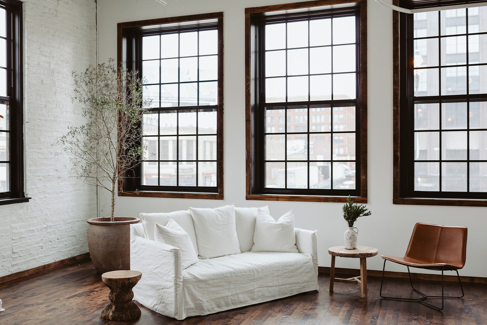 Cozy interior with white sofa, wooden chair, and large windows.