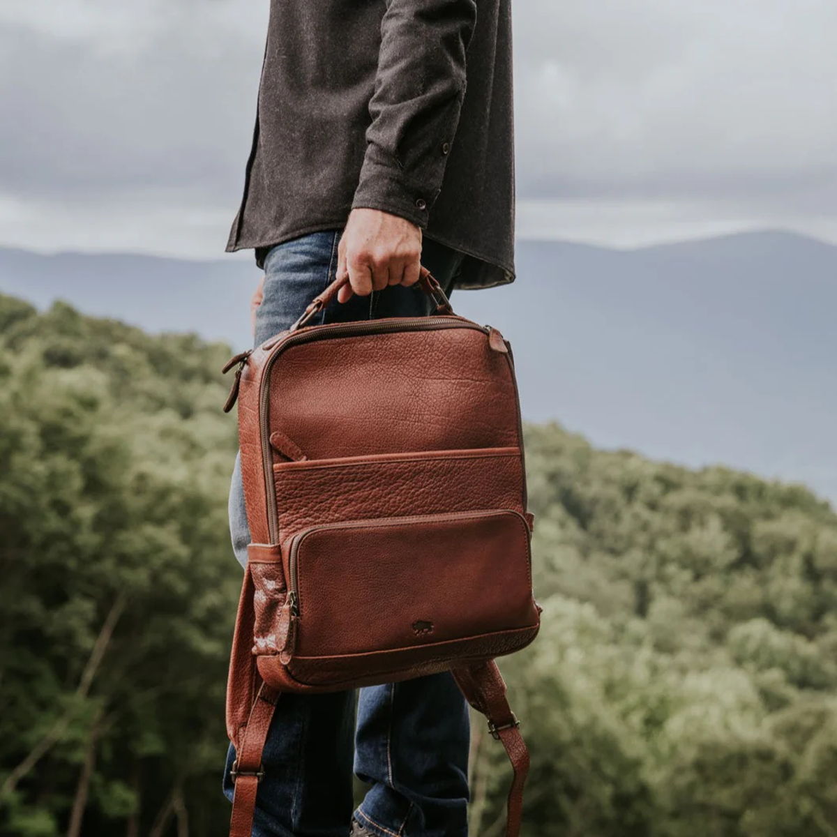 Man holding a Buffalo Jackson Roosevelt full-grain buffalo leather backpack on a mountain overlook