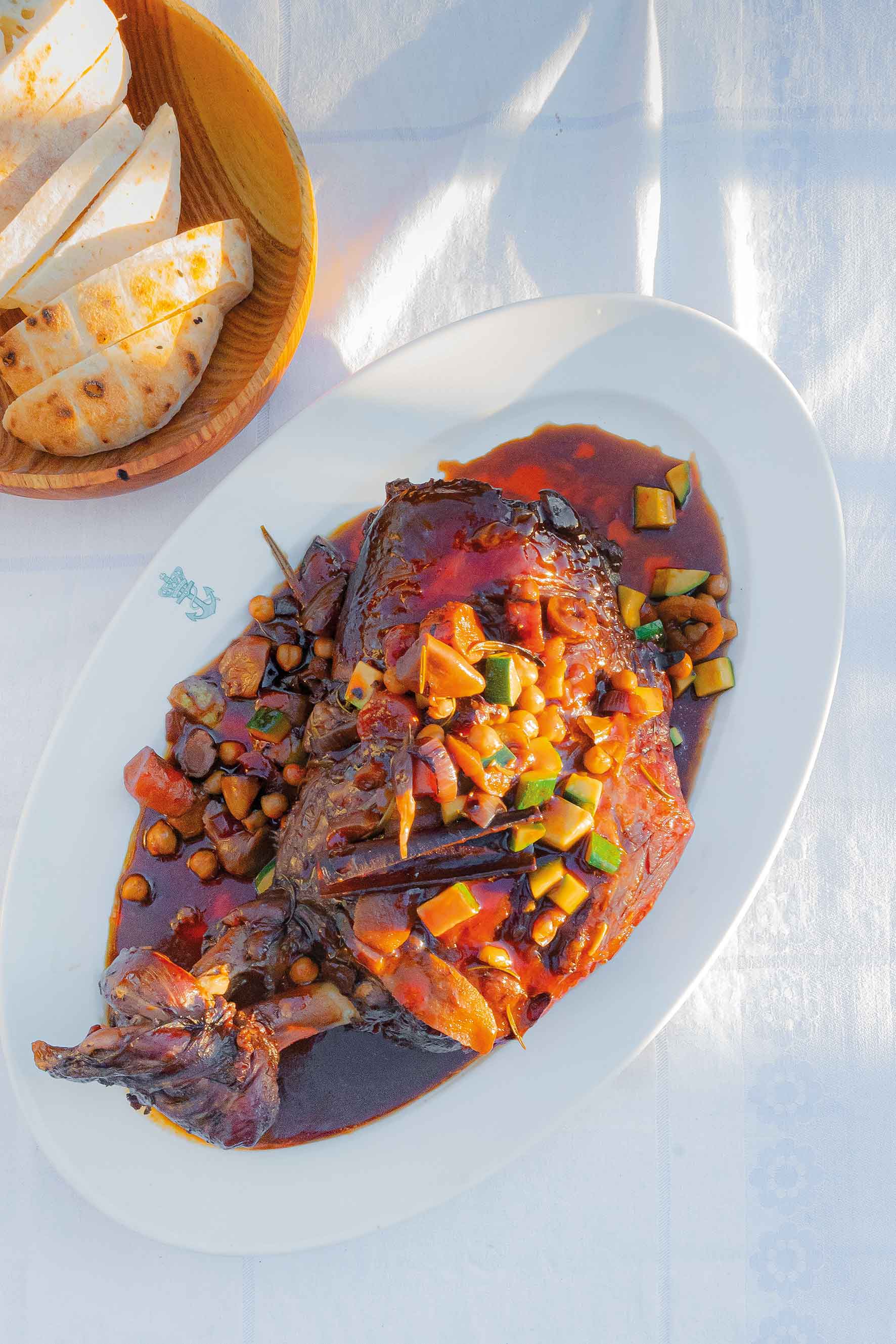 A whole fish dish garnished with vegetables and served with bread.