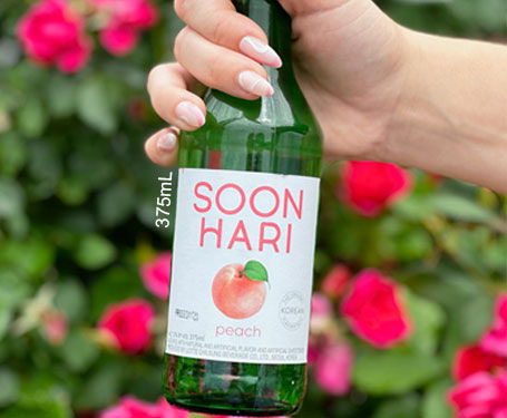 A hand holding a bottle of Soon Hari drink in a flower garden.