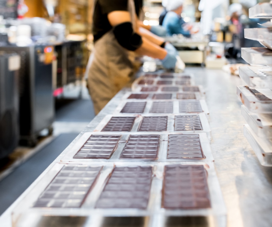 Person working in a chocolate workshop, arranging chocolate pieces on a table.