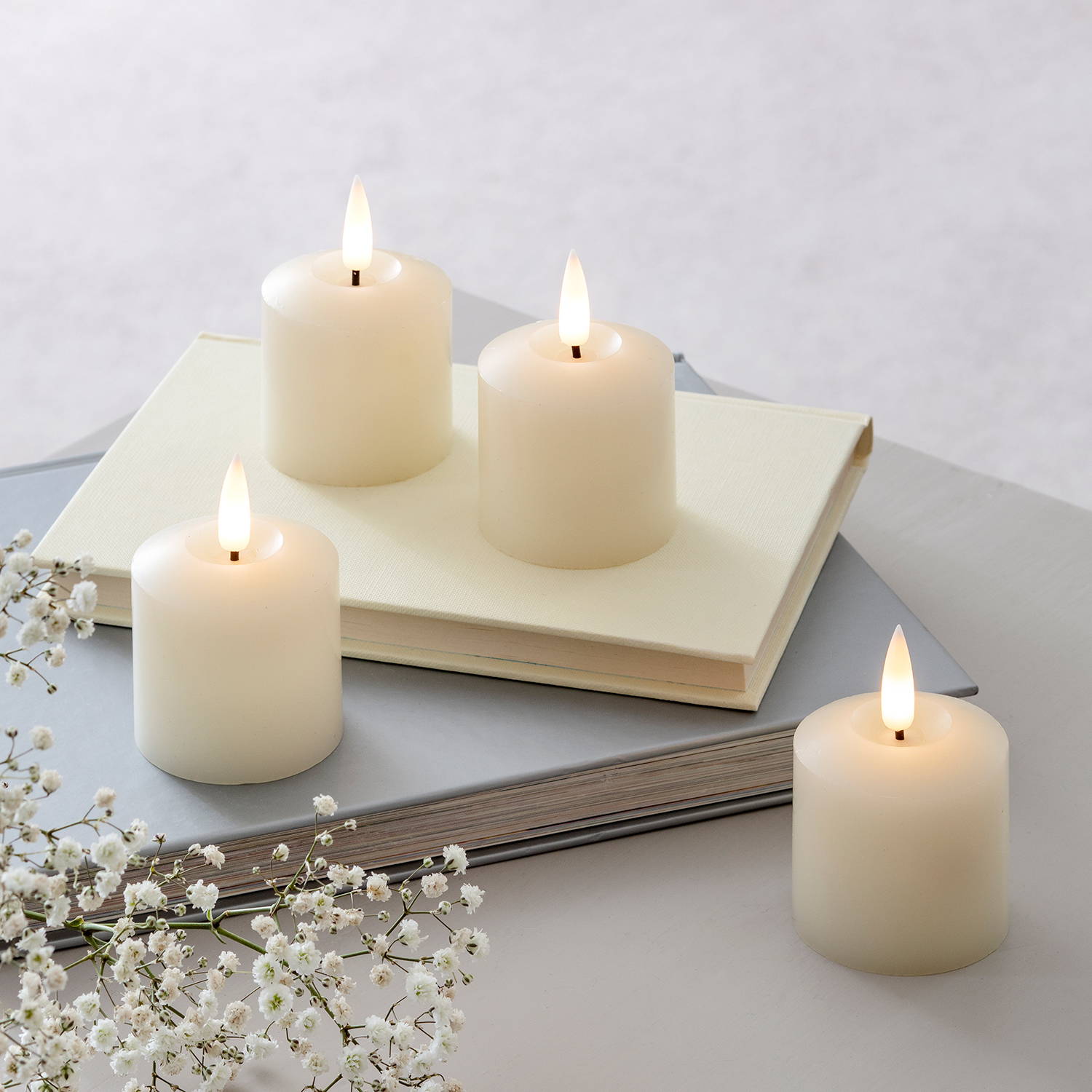 4 Ivory LED votive candles on top of 2 books with some dried flowers.