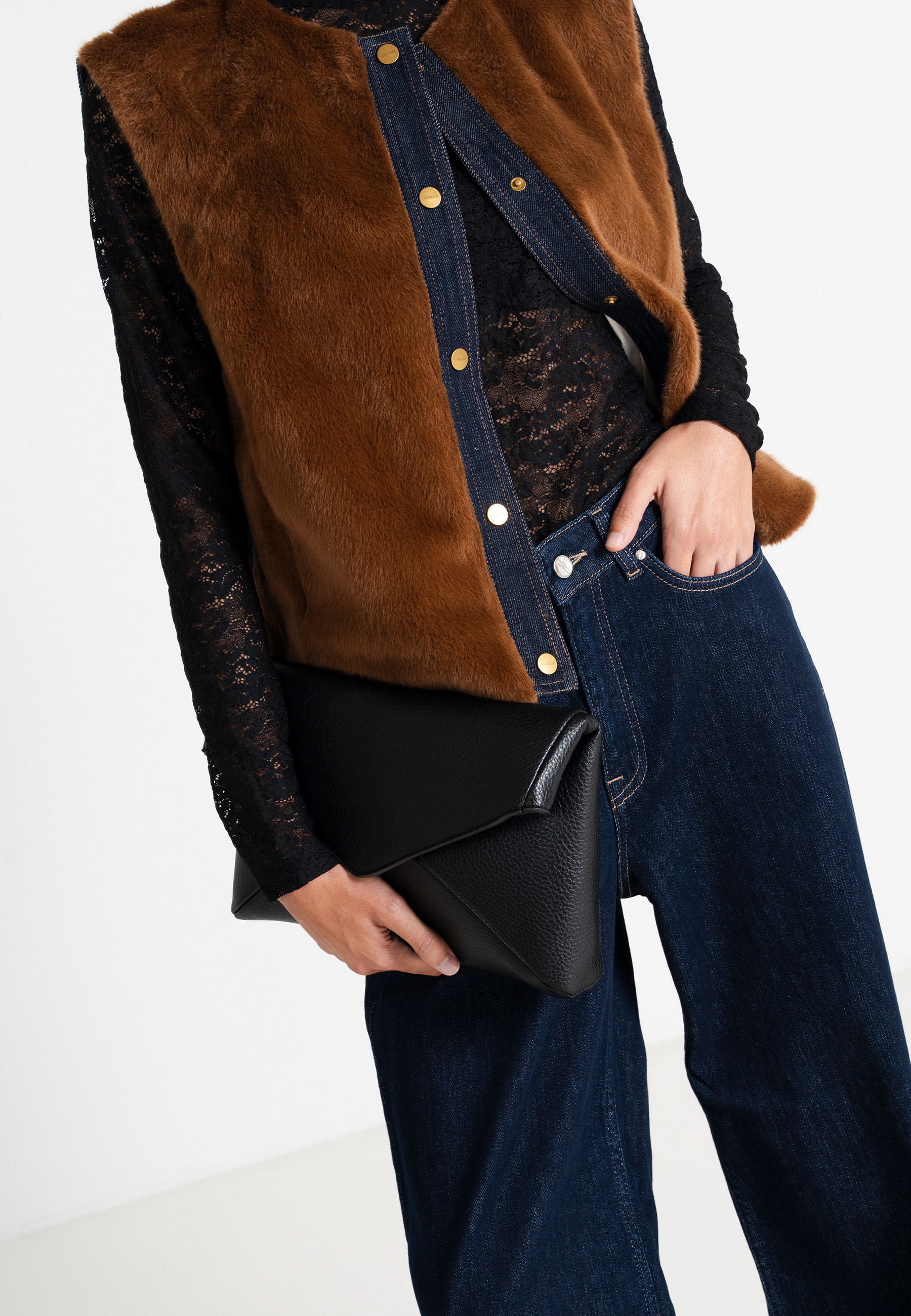 Person wearing a brown fur vest, black top, and holding a black clutch.