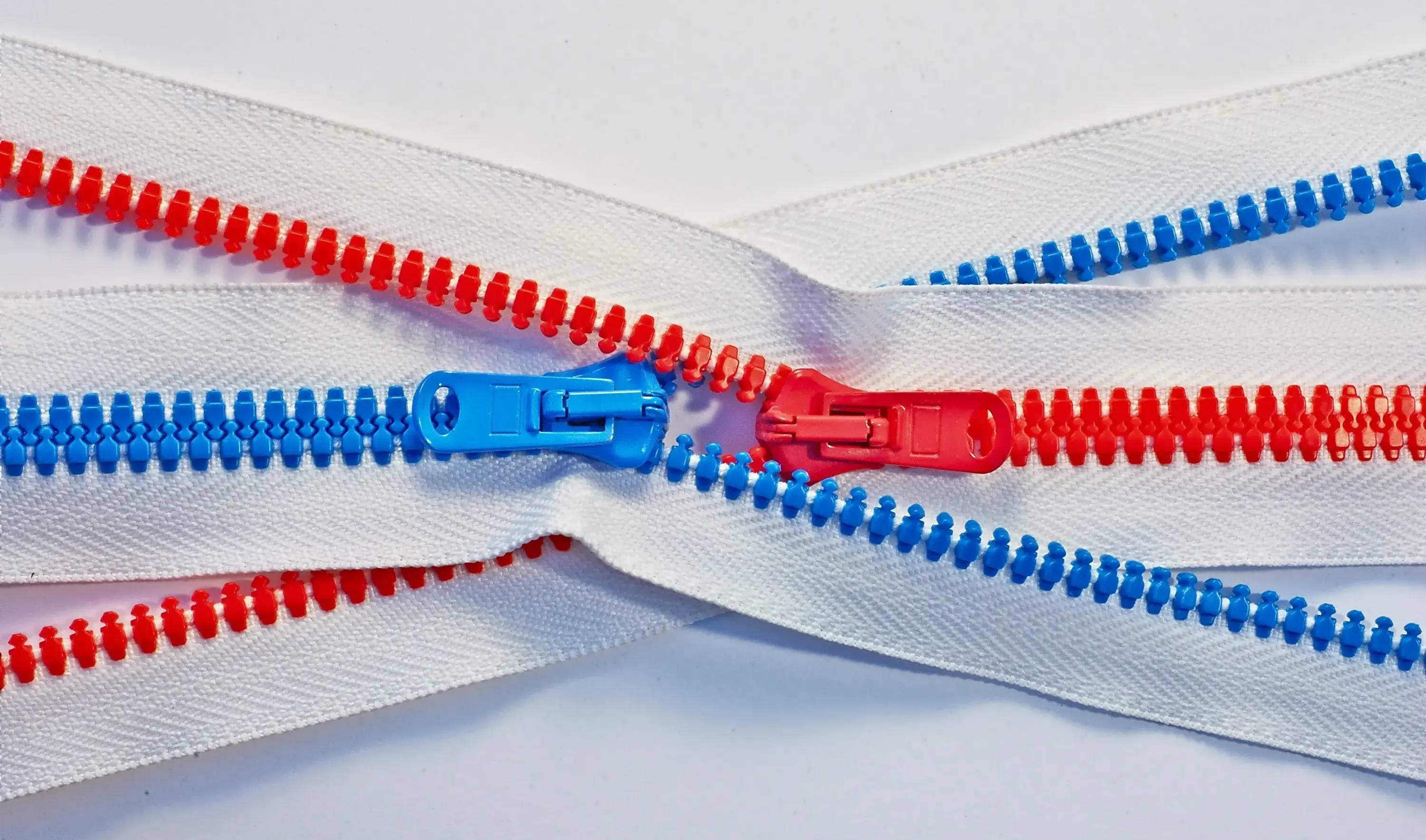 Two zippers zip into each other, one red and one blue. Image by Tomas Sobek. 