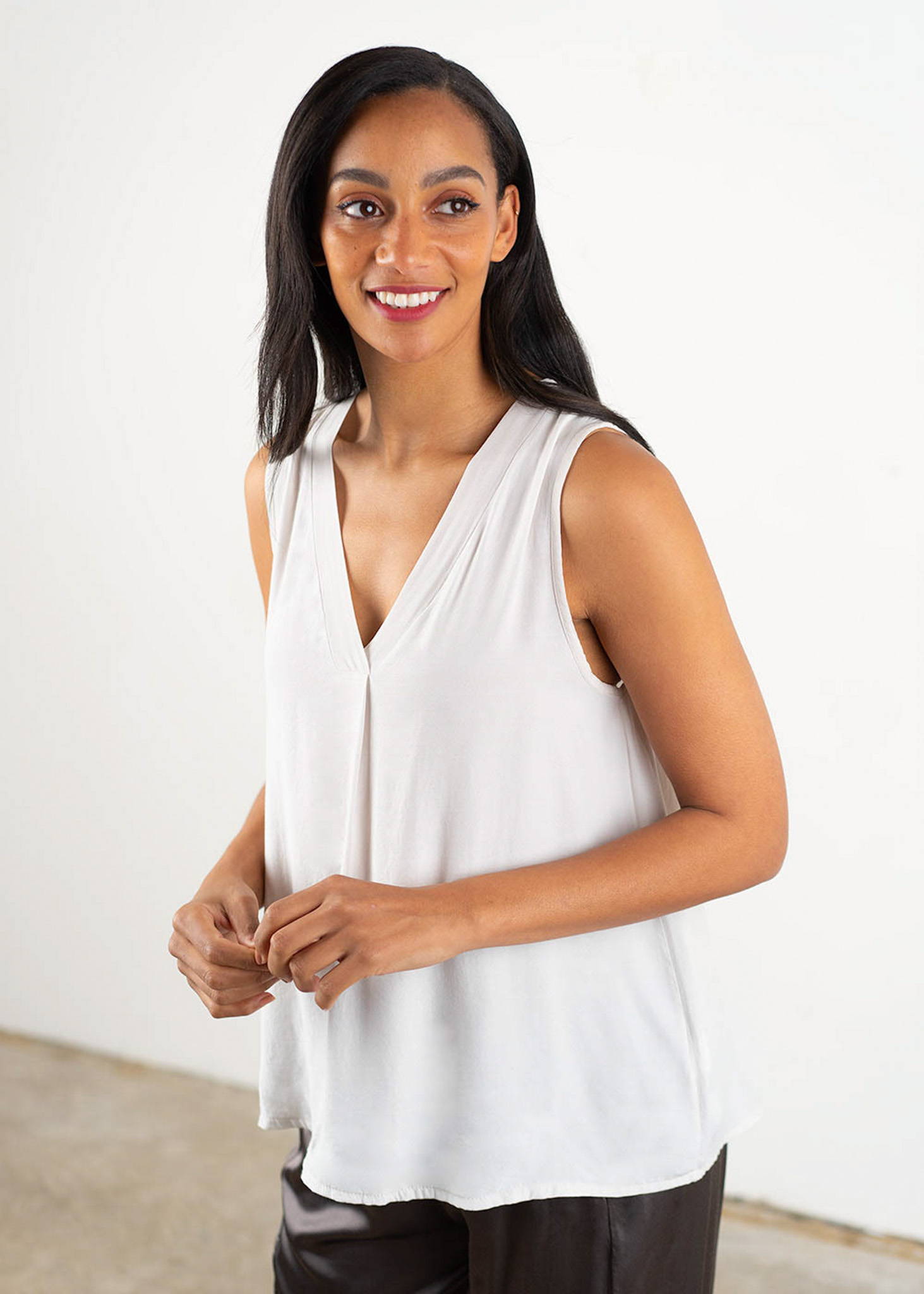A model wearing an off white sleeveless, v neck top and black trousers.