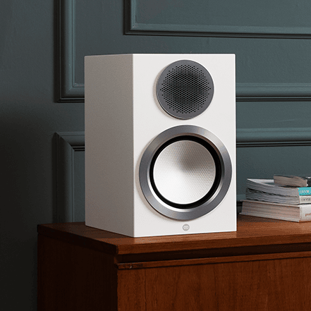 White speaker on a wooden surface with books in the background.