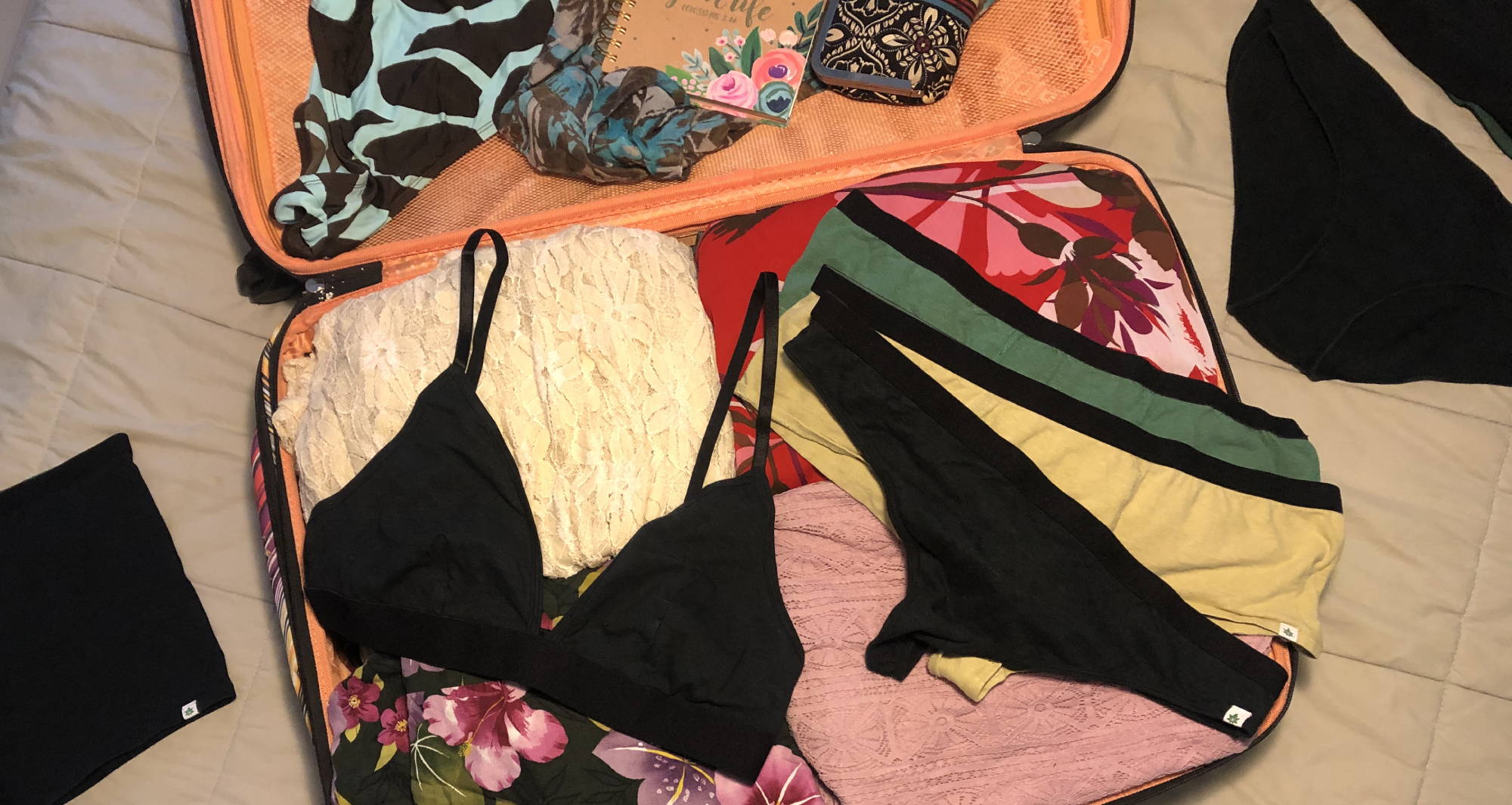 Open suitcase full of clothes with a black bralette and black thong laid on top.