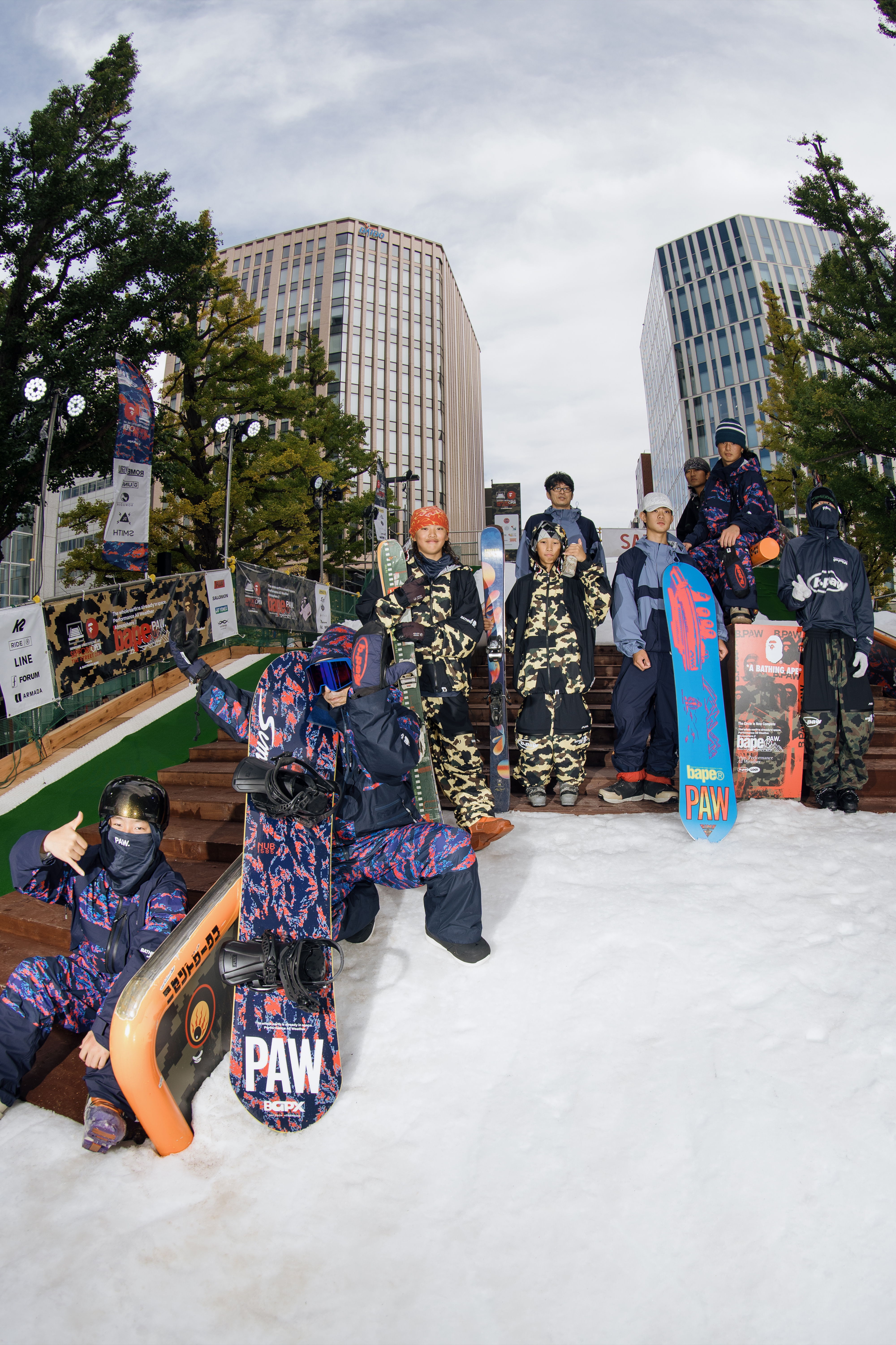 Group of snowboarders posing in a snowy urban setting.