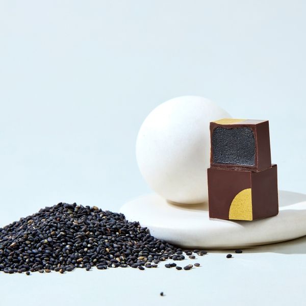 Black sesame seeds, a round white object, and a chocolate square on a plate.