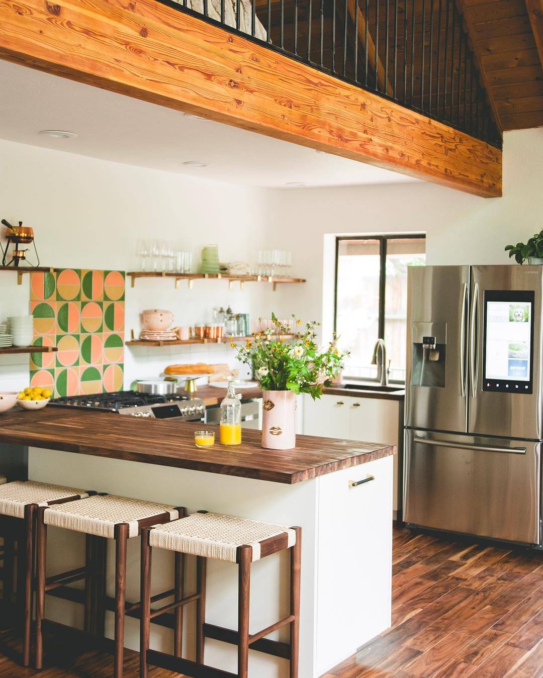 A kitchen with wooden floors and a stainless steel refrigerator, showcasing retro pink and green tiles.