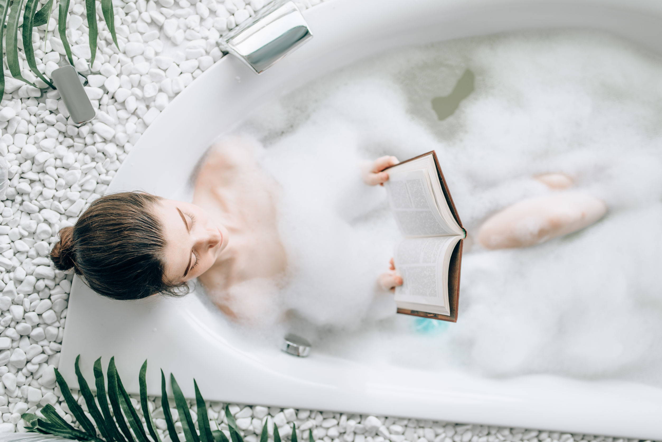 Woman reads a book as she relaxes in a bubble-filled bathtub