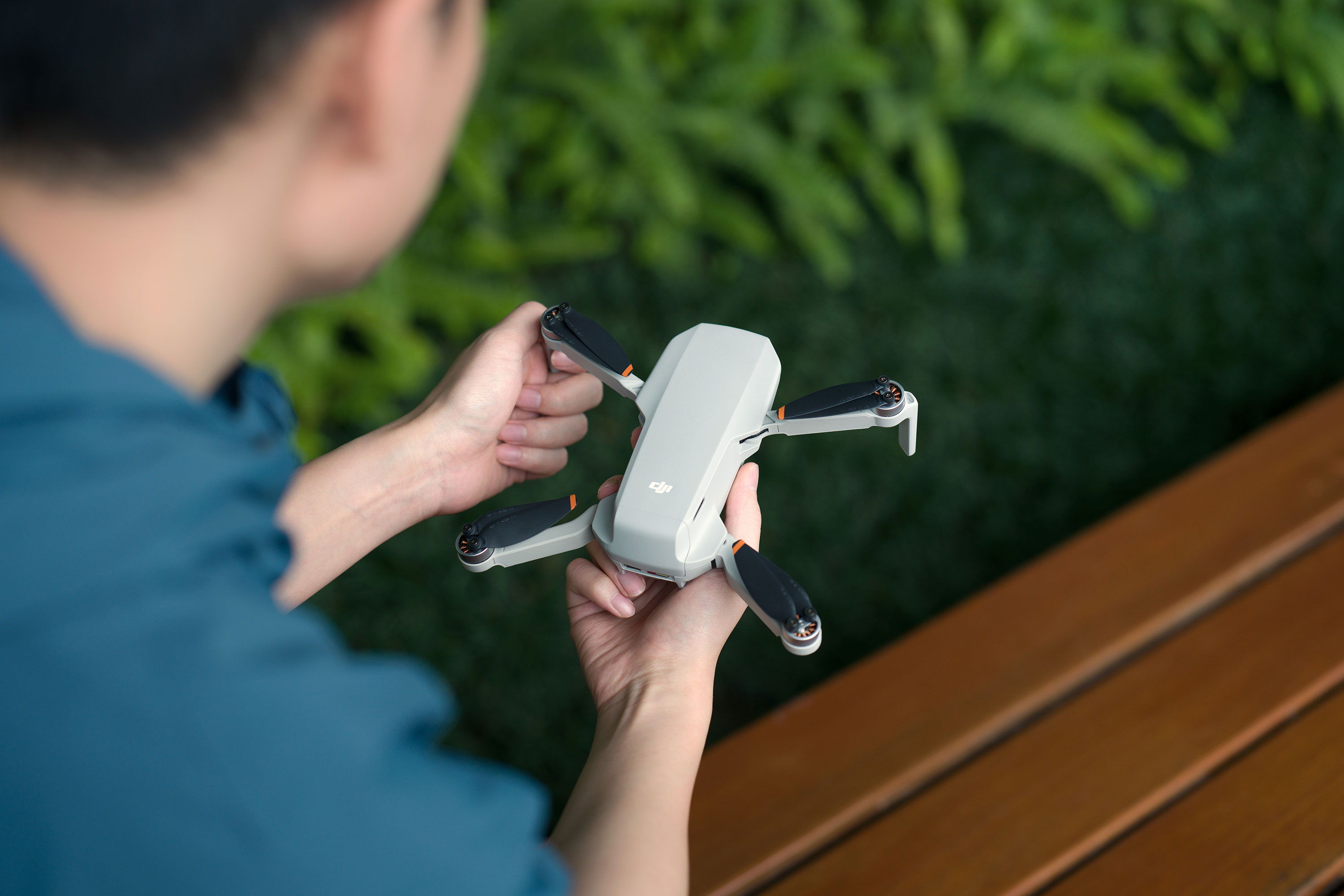 Person holding a DJI Mini 4K drone while sitting on a wooden bench.