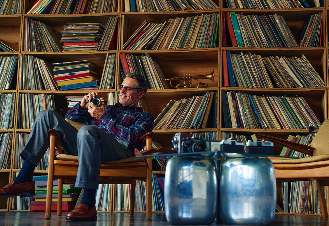 A man sits in a chair, surrounded by vinyl records and gas canisters.