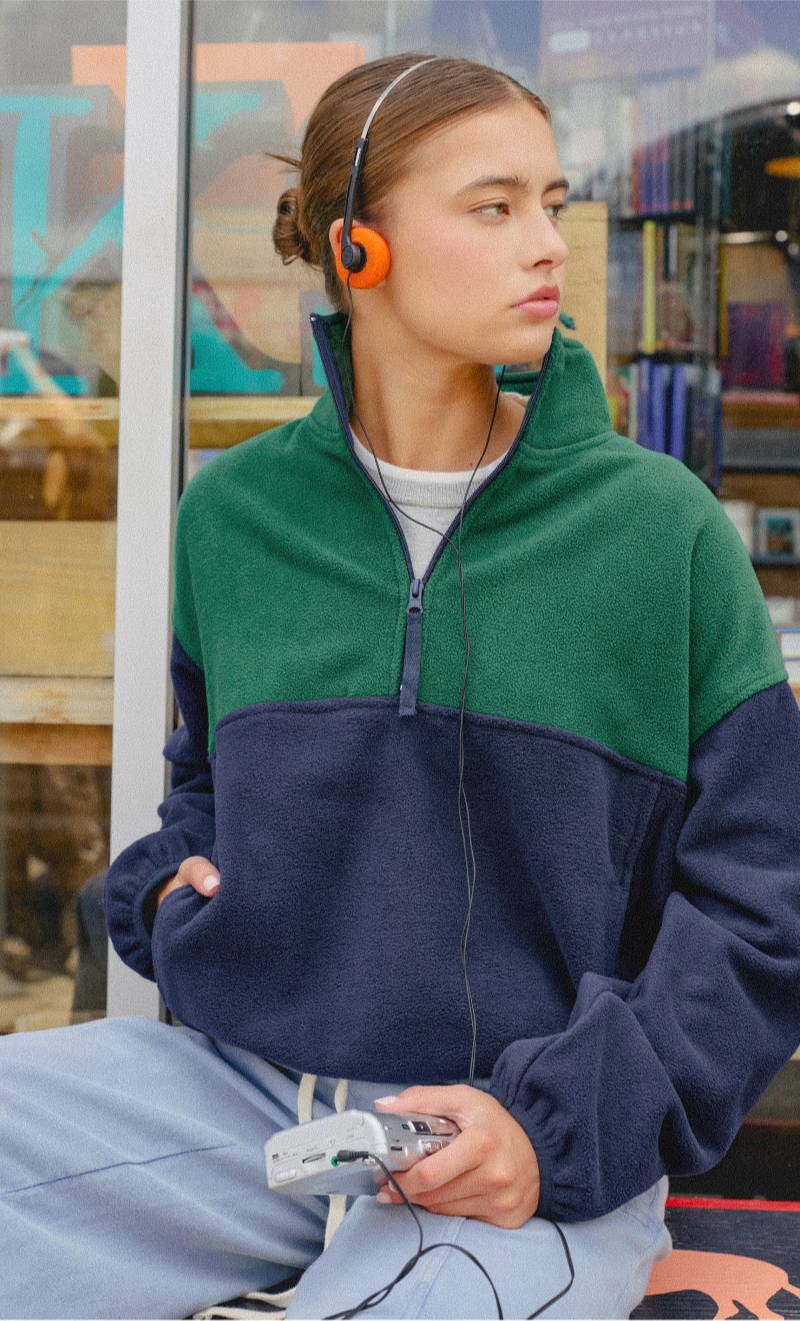 Young woman in a green and navy pullover, wearing headphones and holding a game controller.