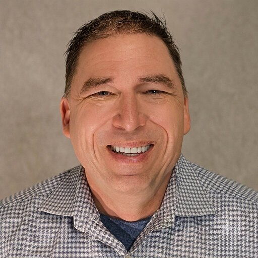 Smiling man wearing a checkered shirt against a neutral background.