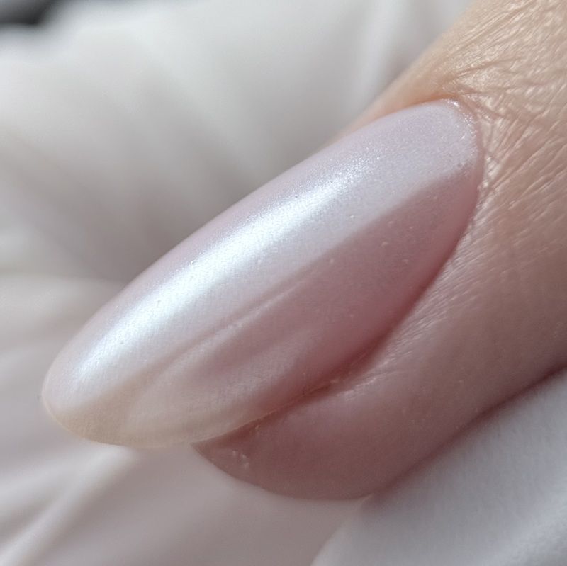 A close-up of a manicured nail with a glossy, iridescent finish.