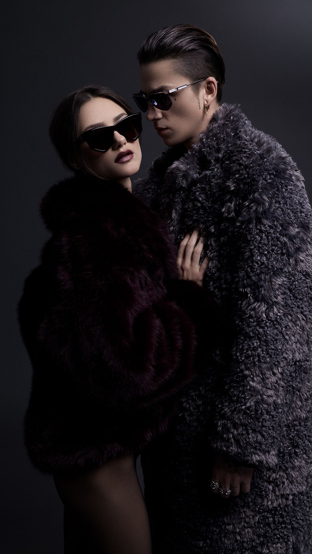 Two stylish individuals in dark fur coats and sunglasses.