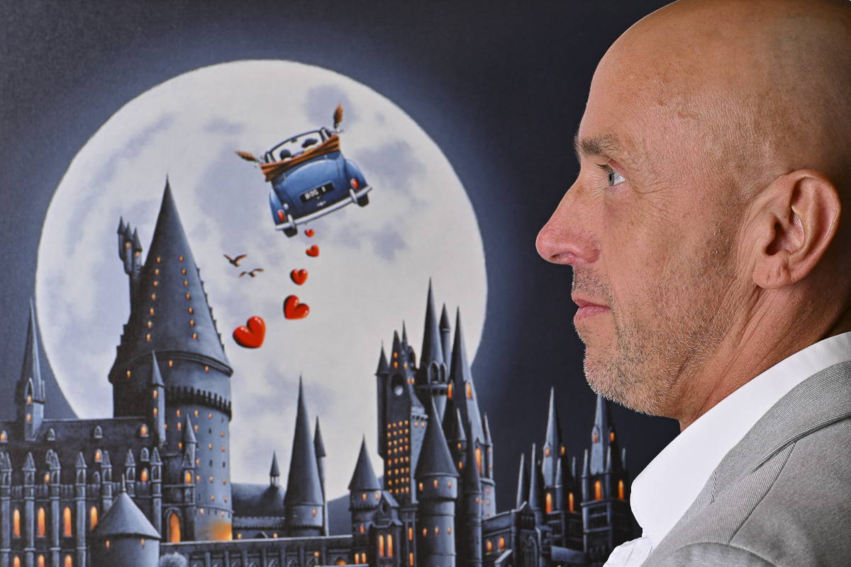 Prints of David's artwork depicting a flying car trailed by red hearts. The foreground is a magical castle inspired by Hogwarts, all bathed in the light of a large mesmerising full moon in the background.