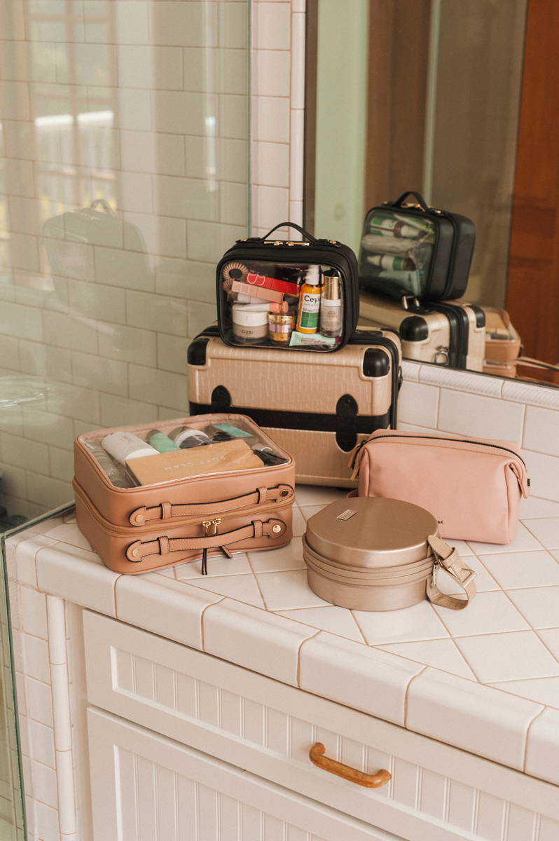 CALPAK Clear Cosmetics Case in Caramel, Baye Mini in Gold, Hue Toiletry Bag in Pink Sand, Vanity Case in Trnk Nude, and Mini Clear Cosmetics Case in Black.