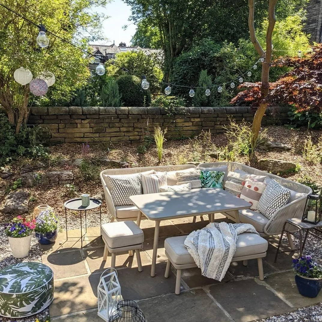 An outdoor seating area with festoon lights, hanging lanterns, pillows and a blanket.