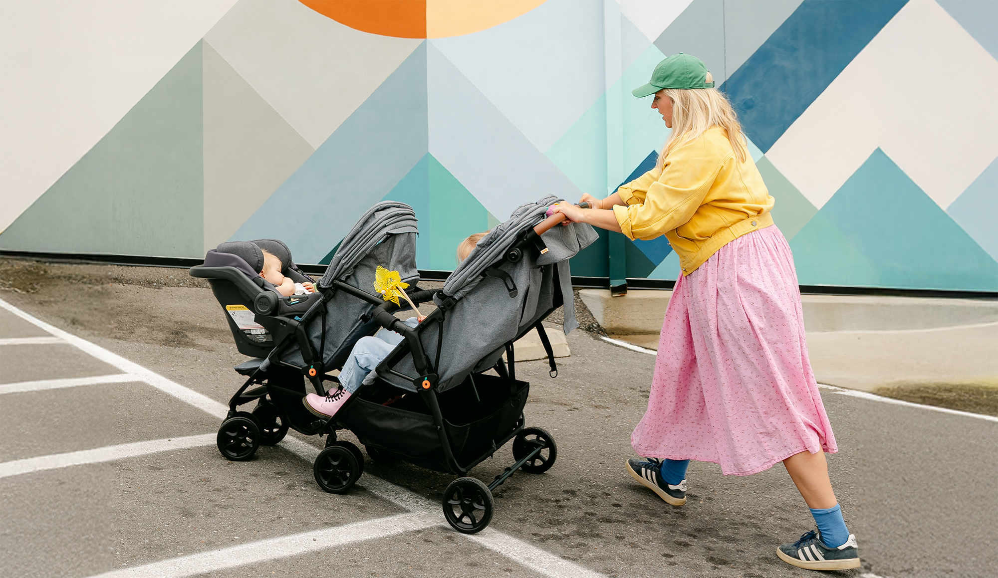 Person pushing a double stroller with children in a colorful outdoor setting.