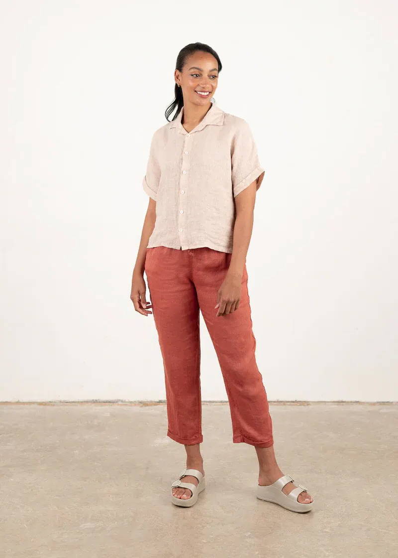 A model wearing a blush pink boxy shirt with shortsless, terracotta linen tapered trousers and off white platform slides