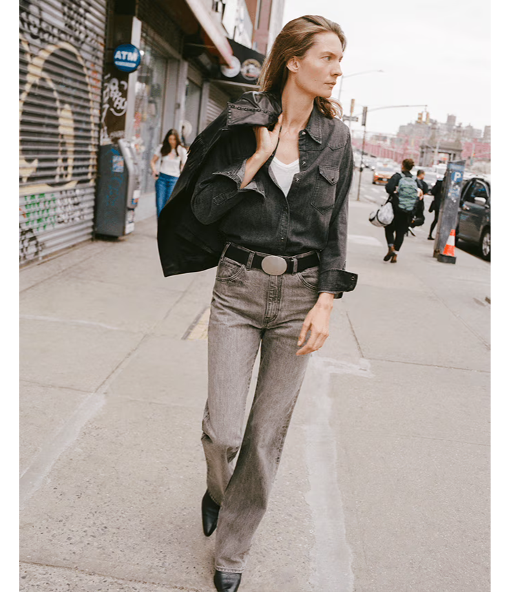 Model walking on a city street wearing a black jacket and gray pants.