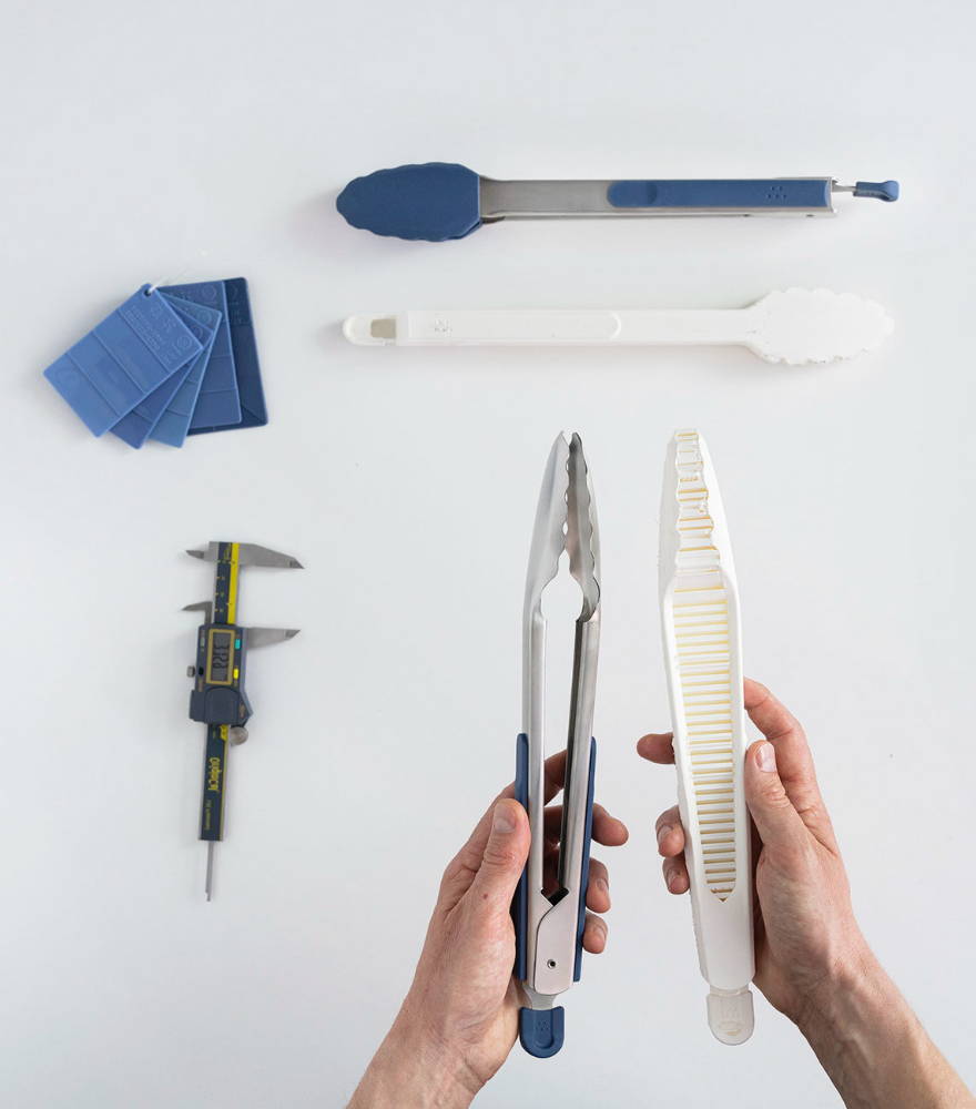 Hands holding a set of Misen Tongs and a 3D printed prototype on a white background. Calipers and color swatches are also visible.