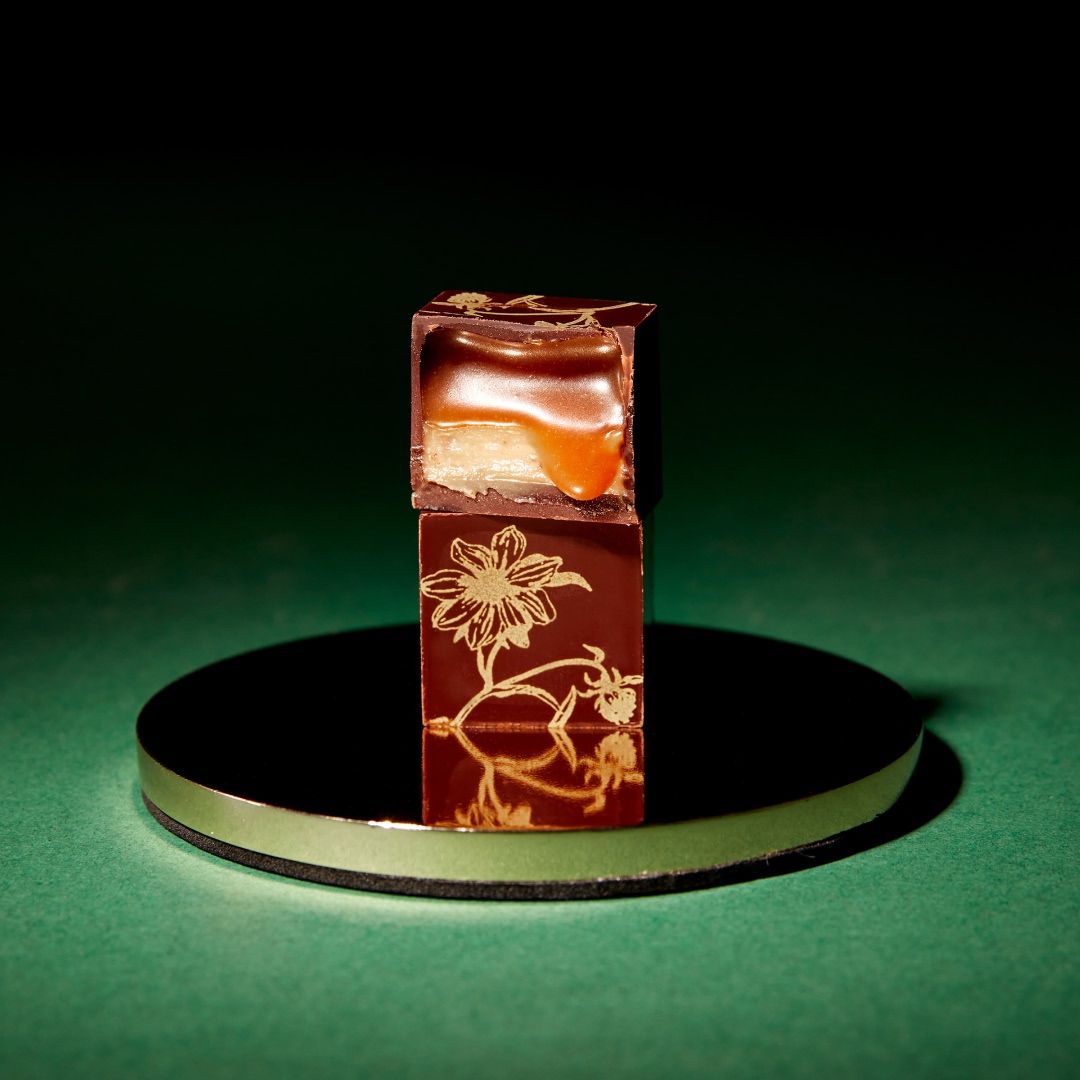 A chocolate cube with caramel filling on a reflective surface.
