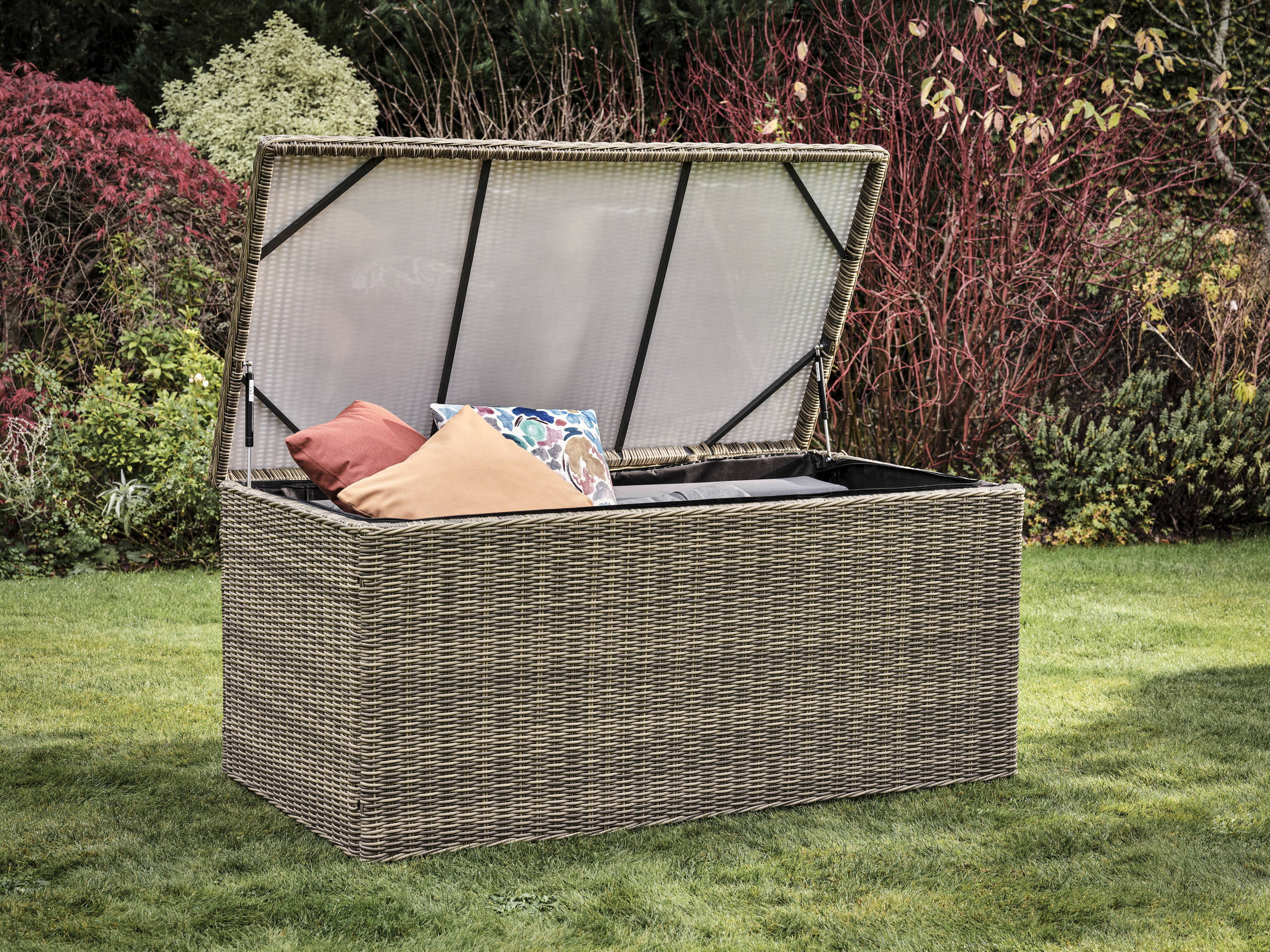 Open rattan storage box filled with cushions in a garden.