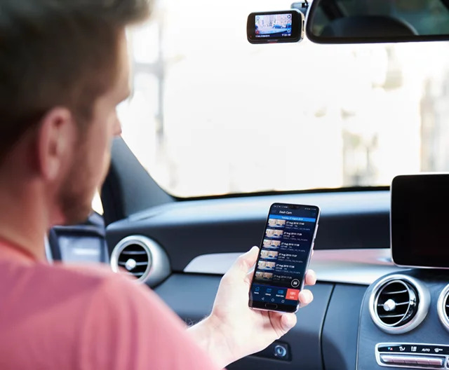 Person using a smartphone inside a car. Dashboard visible in background.