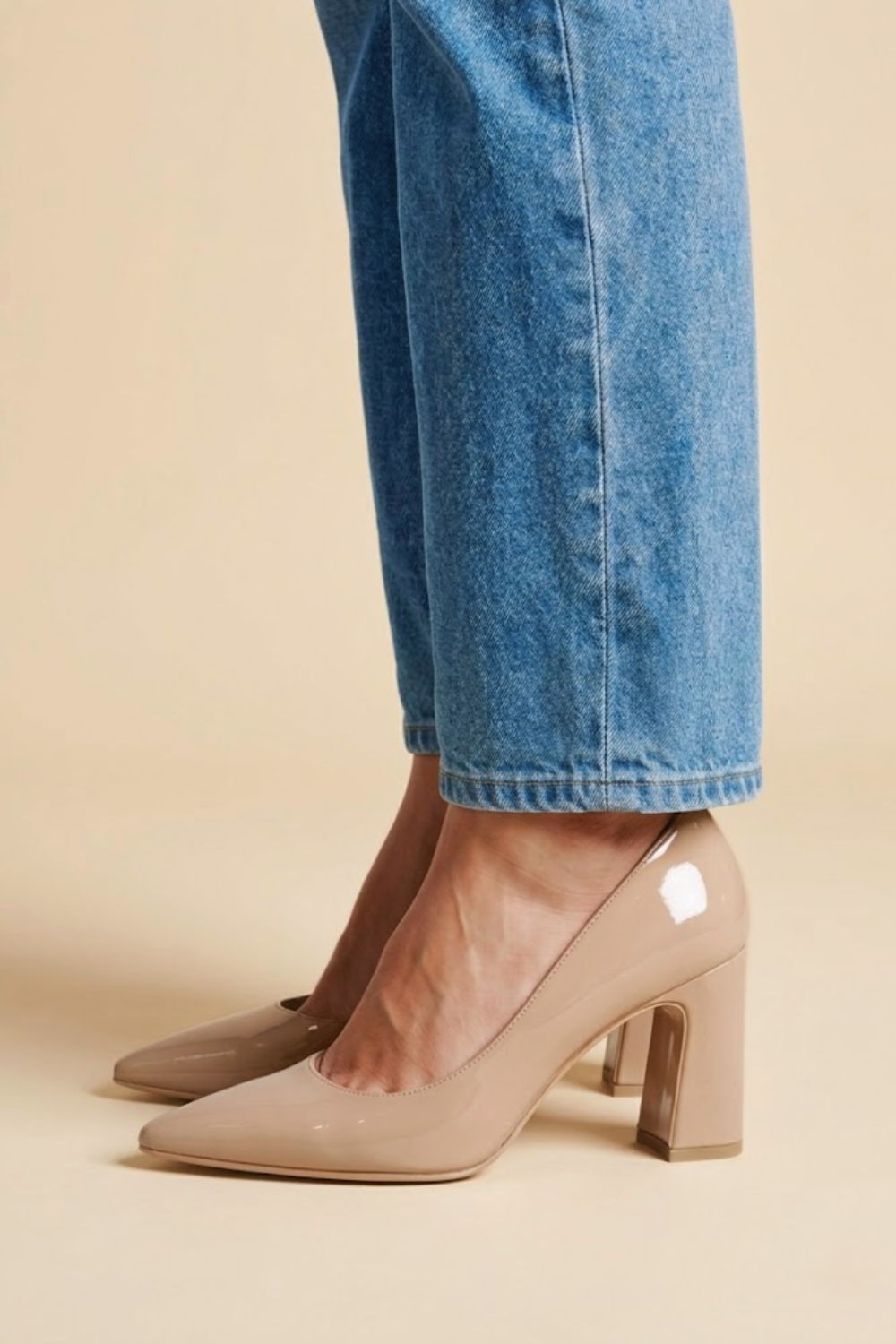 Beige high-heeled shoes worn with blue jeans against a neutral background.