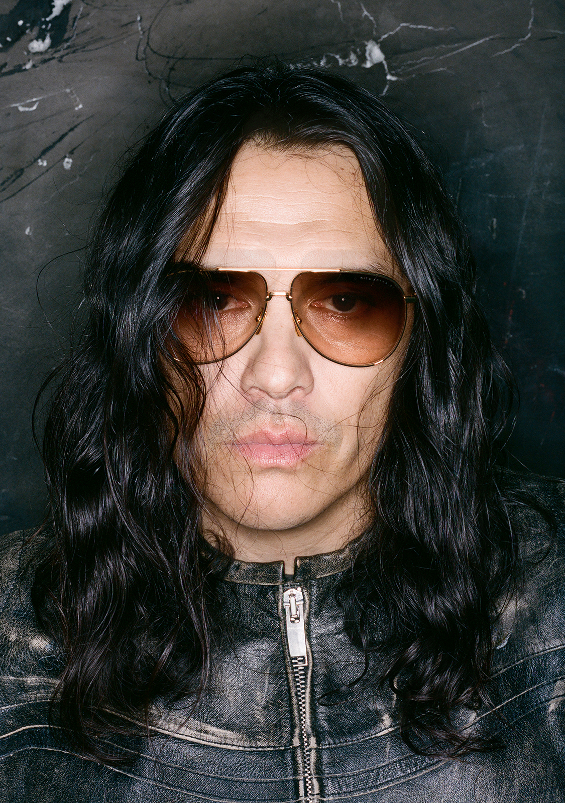 Man with long black hair wearing sunglasses and a leather jacket.