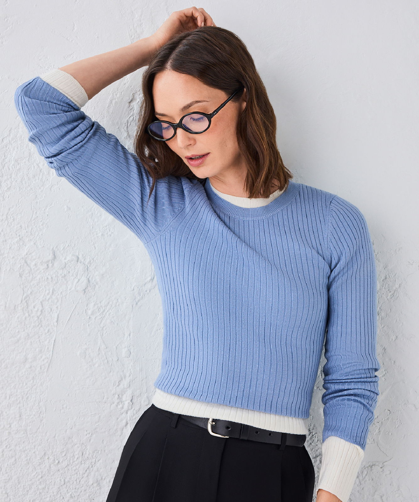 Woman in a blue sweater and glasses, posing against a light background.
