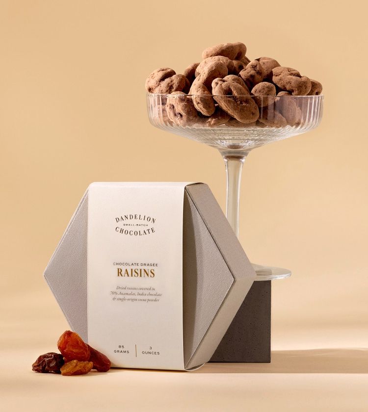 Chocolate-covered raisins in a glass bowl with packaging nearby.