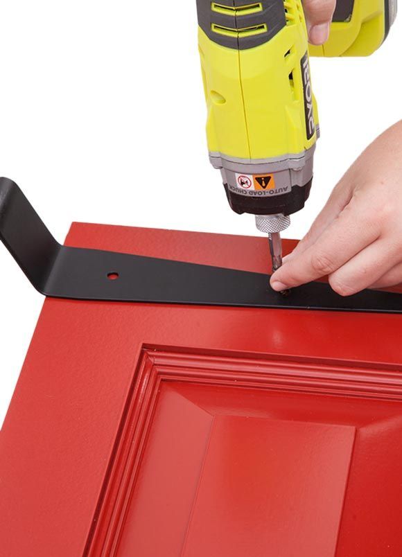 A person using a drill on a red door with a black bracket.