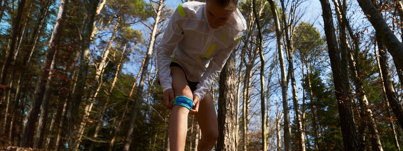 Person adjusting a blue fitness band on their leg in a forest.