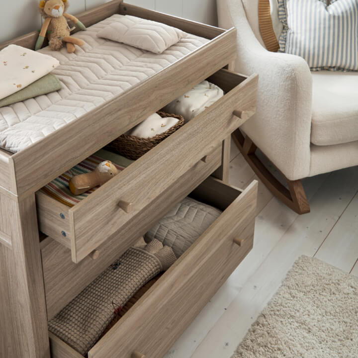 Wooden dresser with open drawers, stuffed toys, and a cozy armchair nearby.