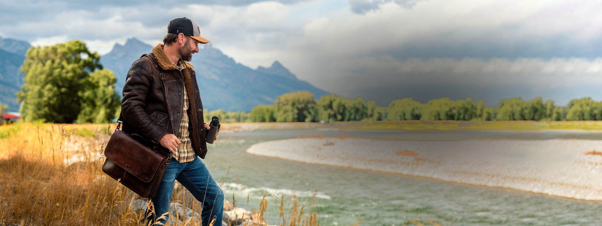 Man in a Buffalo Jackson shearling leather jacket carrying a dark brown leather messenger bag along a mountain river