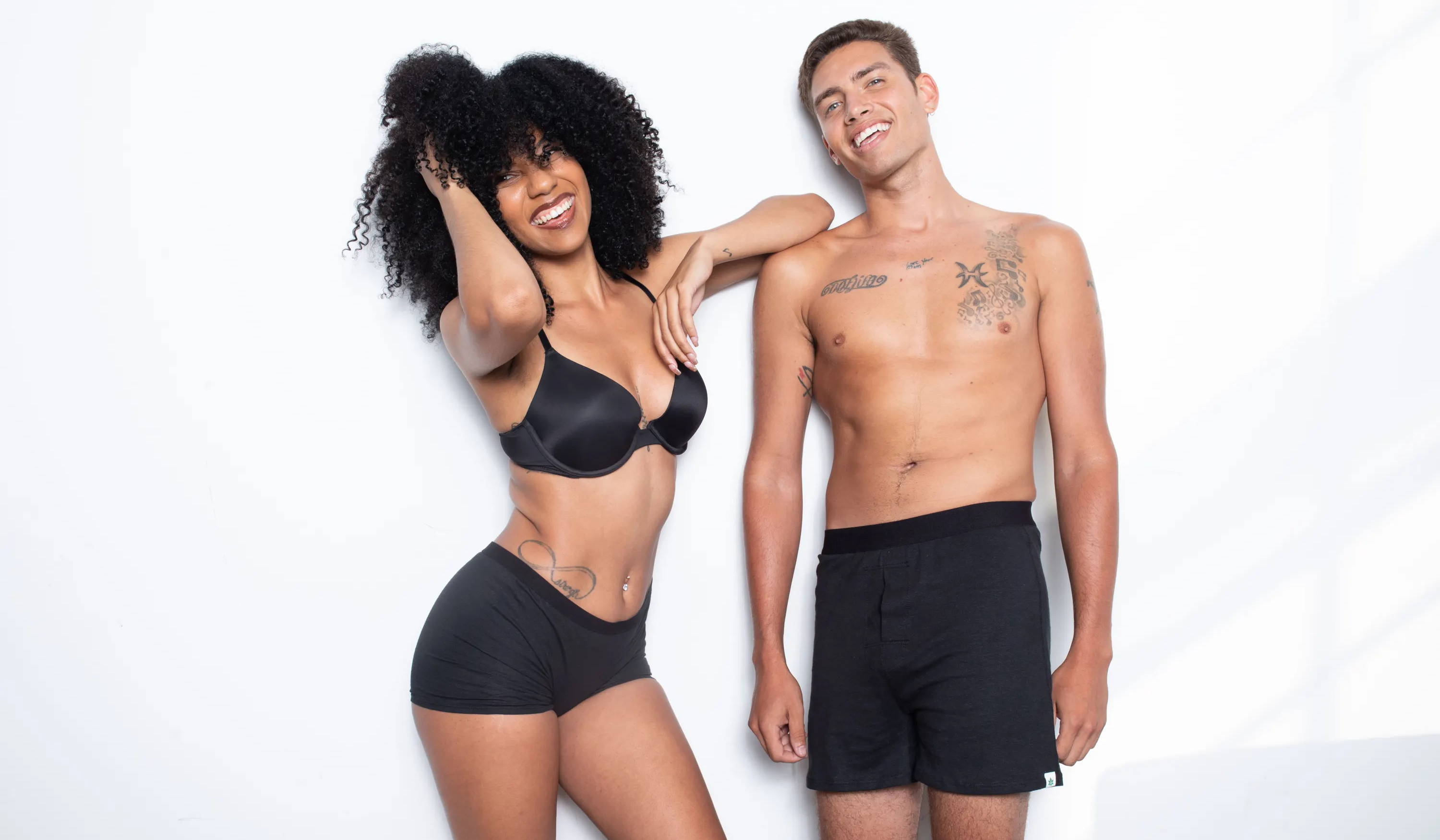 A man and woman stand smiling in WAMA hemp underwear, with the woman scrunching her hair and leaning on the man.