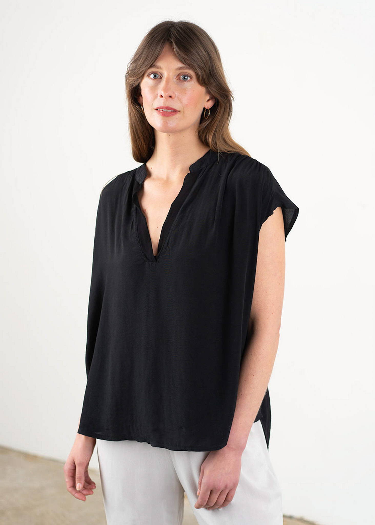 A model weaing a black short sleeved, oversized top with a v neckline.