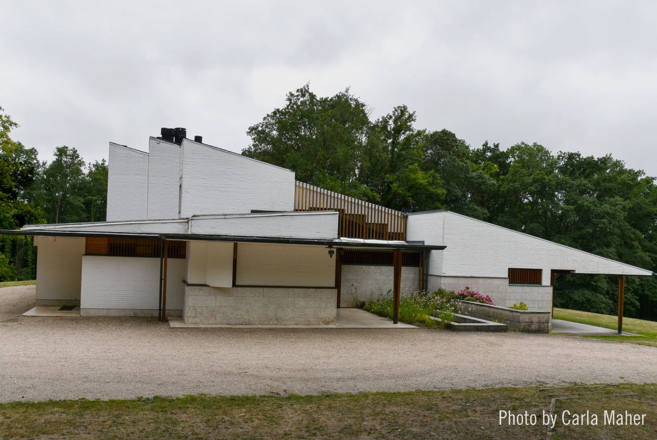 Modern architectural building surrounded by greenery under a cloudy sky.