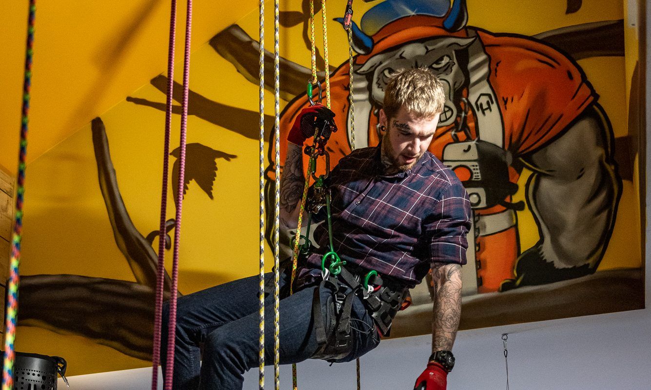 Person rappelling with ropes in front of a colorful mural.