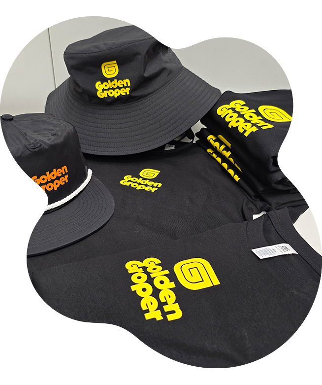 Collection of black Golden Groper branded garments including a wide-brim bucket hat, snapback cap, t-shirt, and long sleeve top, all printed with the yellow and orange Golden Groper logo