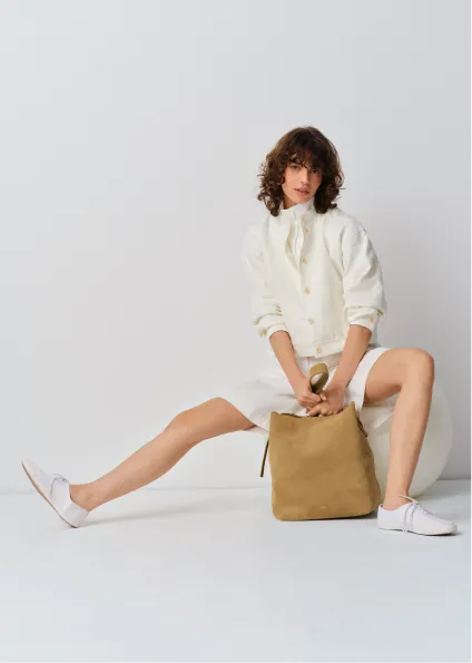 Woman in a white outfit sitting with a tan backpack on a white background.