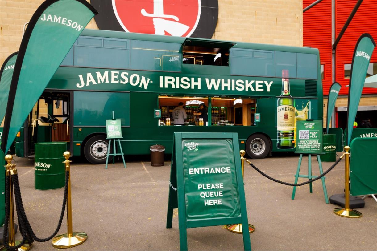A green Jameson Irish Whiskey promotional truck with entrance sign and banners.