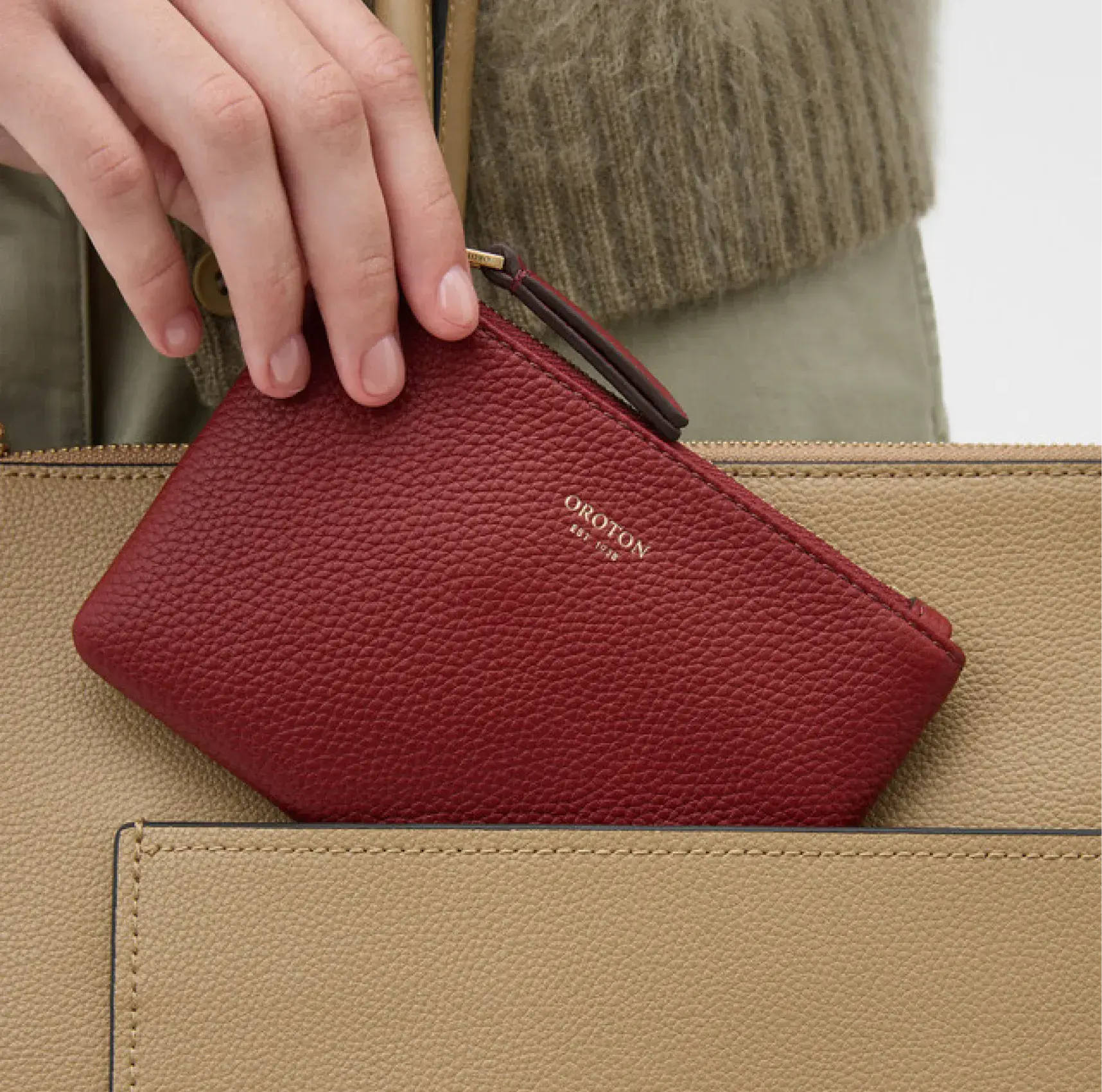A hand placing a red wallet into a beige handbag.
