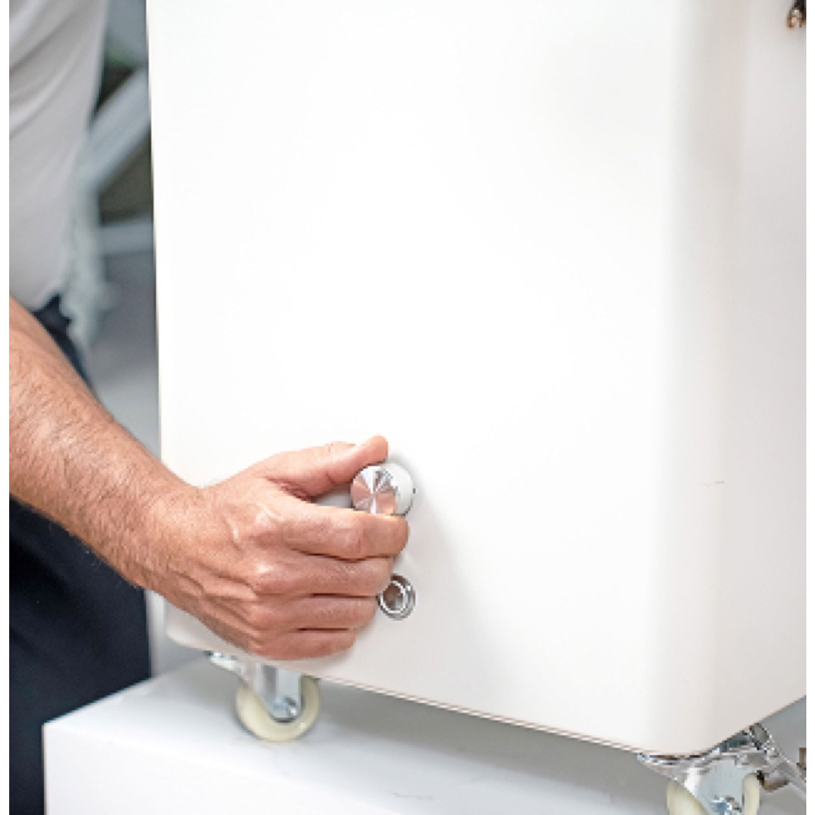 A person adjusting a white appliance with wheels and a knob.