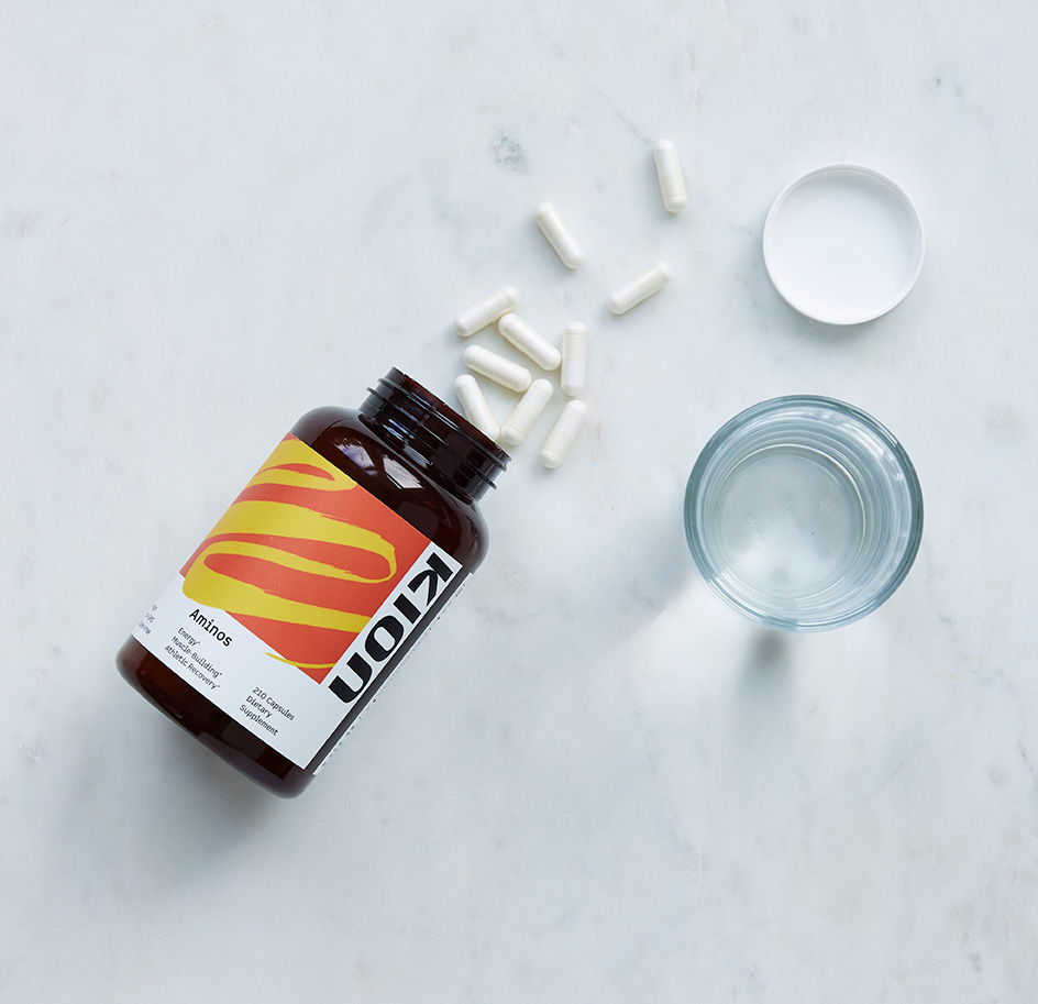 A bottle of vitamins with capsules and a glass of water.