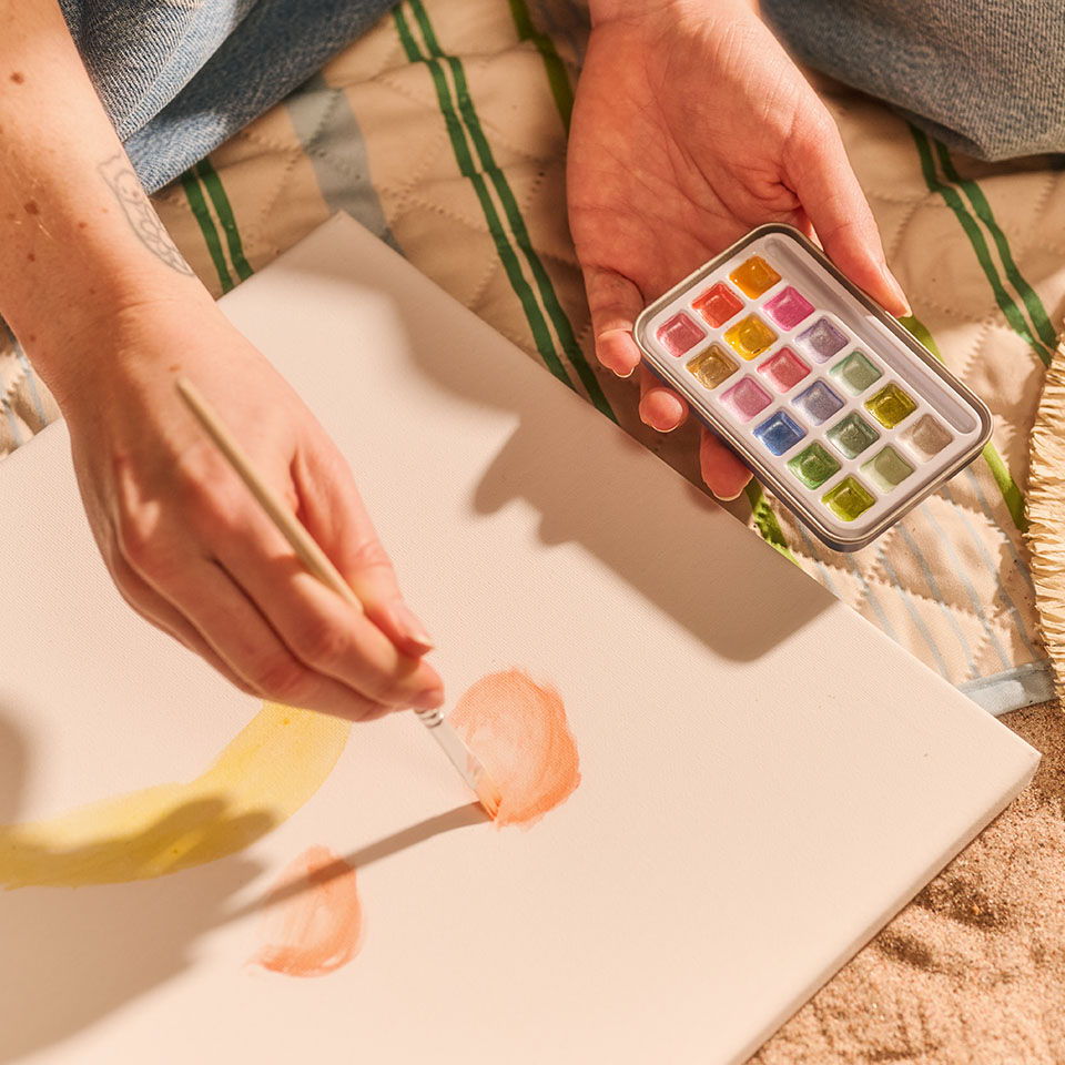 A person painting on a canvas with a watercolor palette.